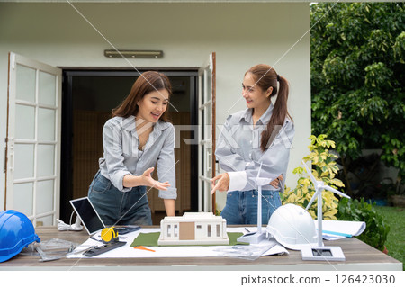 Collaboration and Eco-Friendly Design. Two women engaging in a discussion over a sustainable building model. Collaboration and Eco-Friendly Design. Two women engaging in a discussion over a sustainable building model. 126423030