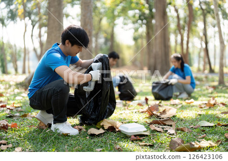 Eco-Consciousness and Active Participation. A young man diligently sorting trash during a community cleanup event, encouraging sustainability. Eco-Consciousness and Active Participation. A young man diligently sorting trash during a community cleanup event, encouraging sustainability. 126423106