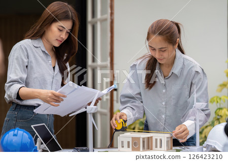 Sustainability and Architectural Design. Two women collaborating on a sustainable building model, discussing eco-friendly solutions. 126423210