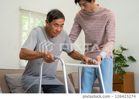 Young man assisting his elderly father with a walker for mobility support. Young man assisting his elderly father with a walker for mobility support. 126423274