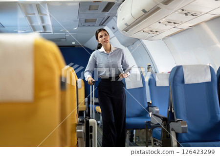 Business travel: Flight attendant assisting a young woman with luggage in airplane Business travel: Flight attendant assisting a young woman with luggage in airplane 126423299