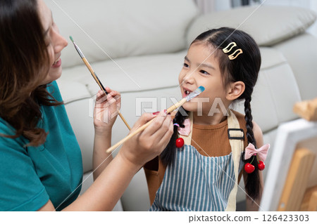 Mother applying paint on daughter face while painting together 126423303
