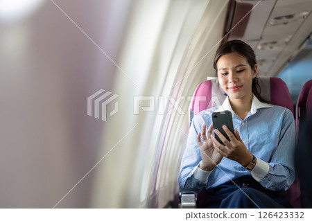 Business travel: Young woman using smartphone on an airplane 126423332