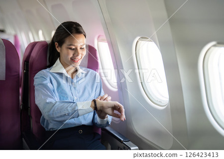 Business travel: Smiling woman checking her watch on airplane Business travel: Smiling woman checking her watch on airplane 126423413