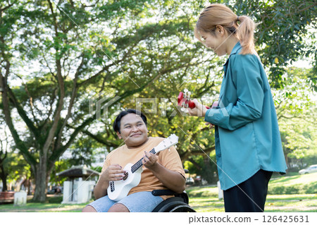 Young man in a wheelchair smiling while playing ukulele with a friend. 126425631
