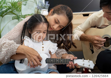 Family Activities and Childhood Learning. A mother helping her daughter learn to play the ukulele. Family Activities and Childhood Learning. A mother helping her daughter learn to play the ukulele. 126425664