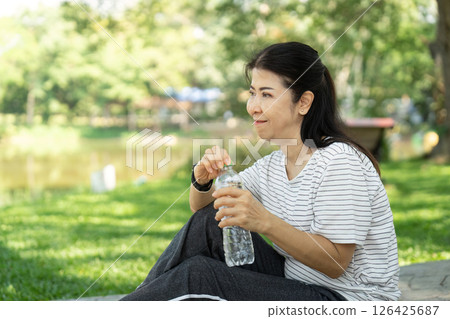Wellness through hydration: Elderly woman drinking water in park 126425687