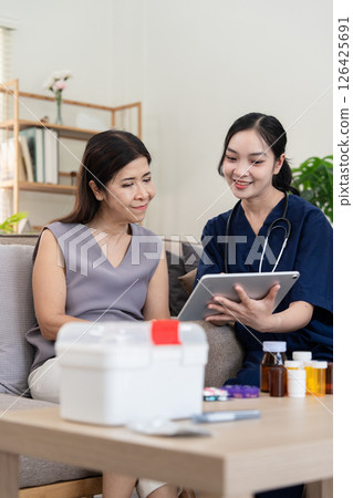 Caregiver discussing health information with elderly client using a tablet during home consultation 126425691