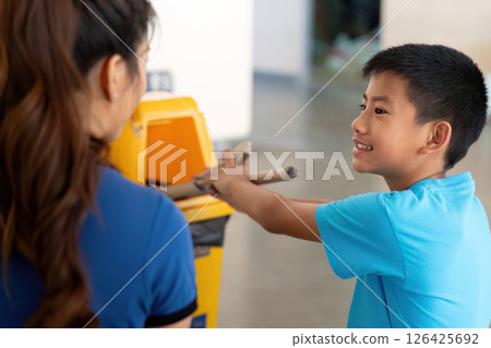 Engaging Youth in Recycling. A boy and a woman enthusiastically participate in waste sorting activities. Engaging Youth in Recycling. A boy and a woman enthusiastically participate in waste sorting activities. 126425692