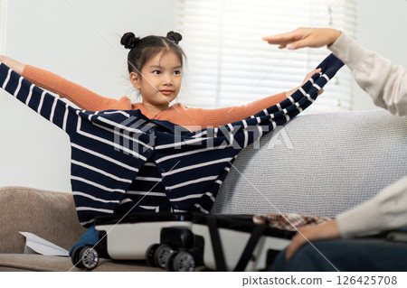 Fun Packing and Adventure. A little girl joyfully tries on clothes while helping with packing for a family trip. Fun Packing and Adventure. A little girl joyfully tries on clothes while helping with packing for a family trip. 126425708