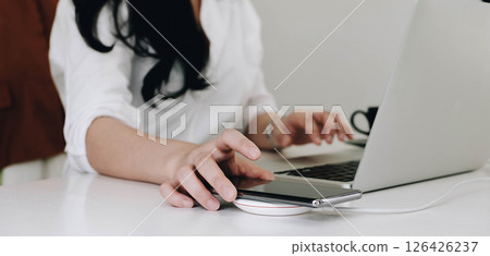 Cropped image of an office woman is charging a smartphone with a wireless charger while typing on a computer laptop. 126426237
