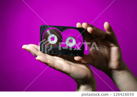 A Pair of Hands Holding a Vintage Tape Cassette Against a Vibrant Purple Background A Pair of Hands Holding a Vintage Tape Cassette Against a Vibrant Purple Background 126428039