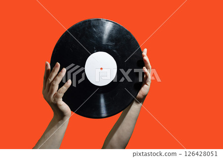 Two hands firmly grasping a vinyl record set against a lively and vibrant background scene 126428051