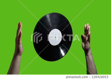 A vinyl record elegantly floating between two hands against a vibrant green background 126428053