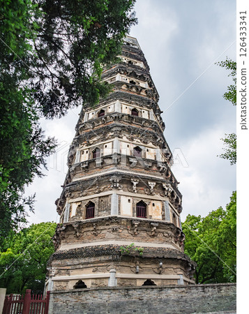 Ancient pagoda stands tall amidst lush greenery in a serene setting under cloudy skies 126433341