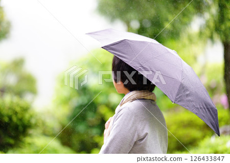一位中年婦女在雨中撐傘站立的背影 126433847