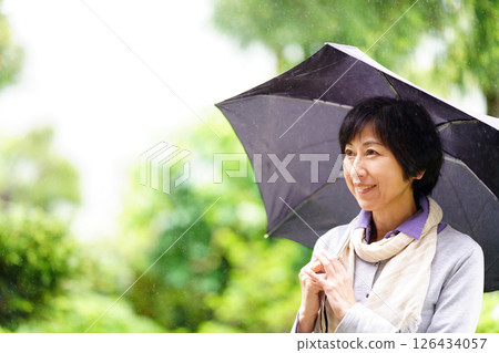 Smiling middle-aged woman standing with an umbrella in the rain Smiling middle-aged woman standing with an umbrella in the rain 126434057
