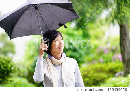 Smiling middle-aged woman standing with an umbrella in the rain Smiling middle-aged woman standing with an umbrella in the rain 126434058