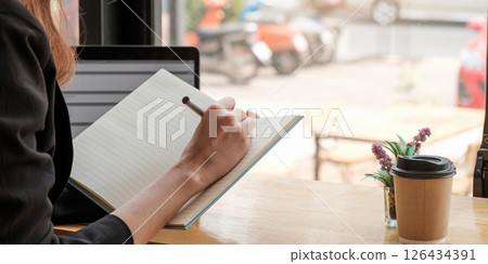 Crop close up of woman study online distant on laptop make note write in notebook sitting on desk at home. Smart female writer or student handwrite in stationery notepad, planning or making list. 126434391