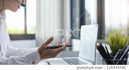 Focused young businessman manager wearing headset with microphone, involved in distant online meeting with colleagues or partners, discussing working issues using video call computer application. Focused young businessman manager wearing headset with microphone, involved in distant online meeting with colleagues or partners, discussing working issues using video call computer application. 126434595