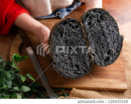 Baker Hand Presenting Homemade fresh baked black charcoal sourdough bread. Showing crumb inside. 126435109
