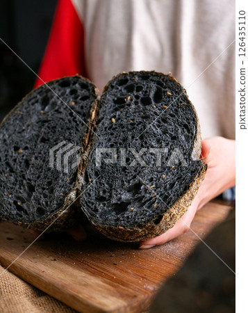 Baker Hand Presenting Homemade fresh baked black charcoal sourdough bread. Showing crumb inside. 126435110