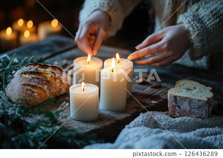 Hands lighting white candles on wooden table with bread and cozy atmosphere for festive setting 126436289
