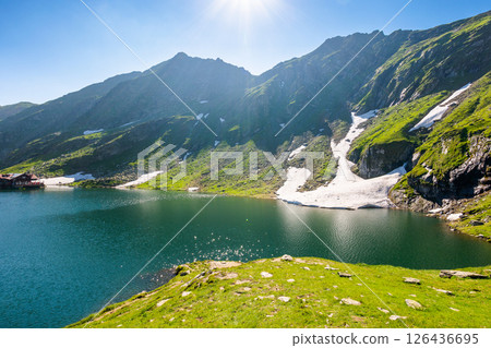 balea lake of romania. alpine landscape of fagaras mountains with pond. sunny weather with clouds on the blue sky above carpathians. snow and grass on the hillside in summer. vacation season 126436695