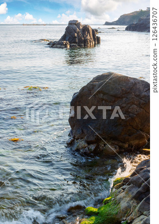 seascape with rock in the water. textured boulder reflecting calm sea surface in morning light. vacation season in summer. sunny weather. fluffy clouds above horizon seascape with rock in the water. textured boulder reflecting calm sea surface in morning light. vacation season in summer. sunny weather. fluffy clouds above horizon 126436707
