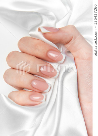 Woman hand showing french manicure on white silk background Woman hand showing french manicure on white silk background 126437260