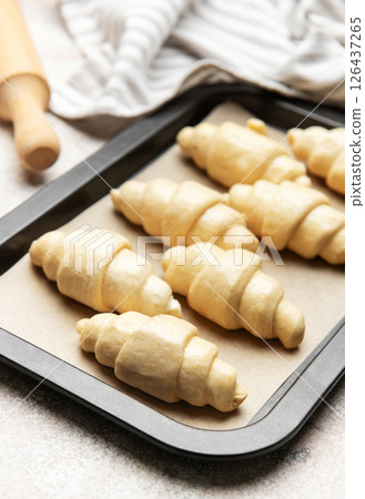 Raw croissants baking on tray with rolling pin and kitchen towel Raw croissants baking on tray with rolling pin and kitchen towel 126437265