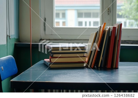 Stacks of school books rest on a blue desk next to a window, allowing natural light to illuminate the study area 126438682