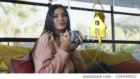 Image of gold house key and key fob over diverse woman dinking tea at home 126440922