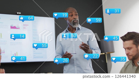 Image of media icons over diverse colleagues discussing work in office 126441340