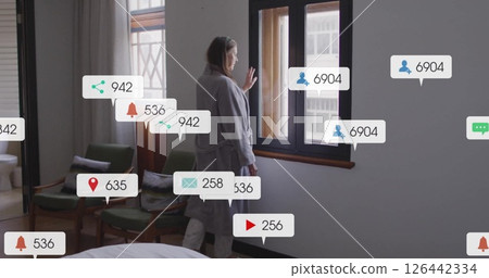 Image of media icons over caucasian woman looking through window Image of media icons over caucasian woman looking through window 126442334