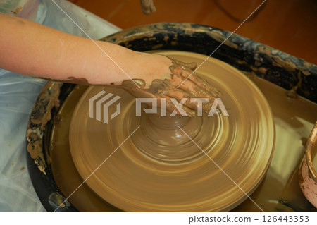 The potter's wheel. A close-up of the hands of a craftsman skillfully working with clay on a potter's wheel, giving it the shape of a clay product The potter's wheel. A close-up of the hands of a craftsman skillfully working with clay on a potter's wheel, giving it the shape of a clay product 126443353