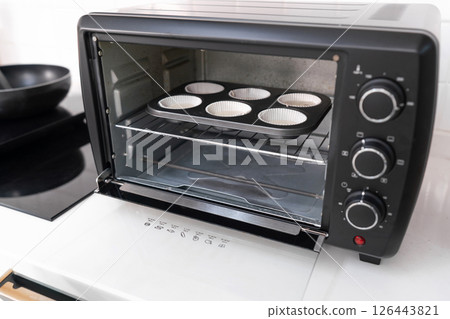 Six-slot muffin tray with batter in a black toaster oven on white kitchen counter Six-slot muffin tray with batter in a black toaster oven on white kitchen counter 126443821