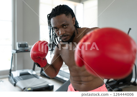 A muscular boxer wearing red gloves train hard in a gym, showcasing focus and determination as he prepare for his next match, surrounded by fitness equipment. A muscular boxer wearing red gloves train hard in a gym, showcasing focus and determination as he prepare for his next match, surrounded by fitness equipment. 126444006