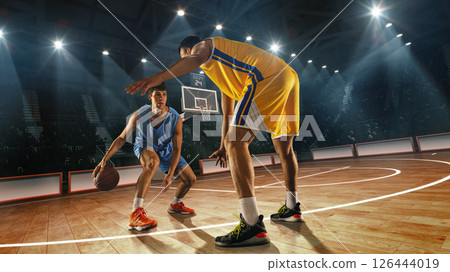 Composite collage. Basketball player in blue dribbles low, facing defender in yellow uniform on 3D basketball court with visible hoop and audience behind. 126444019