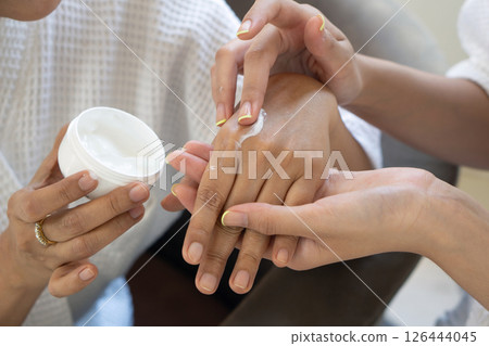 Two women in white robe applying a skincare product into their hand. Close up 126444045