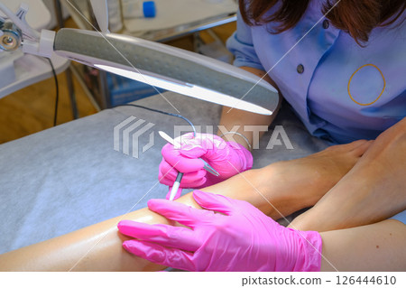 Young beautiful female dermatologist doing hair removal treatment on patient's legs with electrolysis. Epilation and beauty concept. High quality photo 126444610