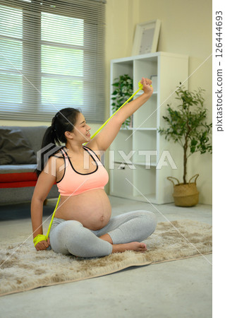Smiling pregnant woman doing a home workout with a stretch band Smiling pregnant woman doing a home workout with a stretch band 126444693