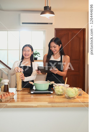 Beautiful asian mother and daughter cooking pasta together in the kitchen Beautiful asian mother and daughter cooking pasta together in the kitchen 126444696