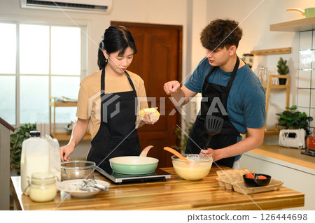 Man and woman wearing aprons preparing pancakes at home Man and woman wearing aprons preparing pancakes at home 126444698
