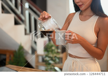 Young woman pouring freshly brewed coffee into a mug in a home kitchen Young woman pouring freshly brewed coffee into a mug in a home kitchen 126444711