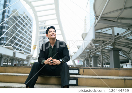 Confident businessman sitting on steps in urban cityscape and looking up with optimism 126444769