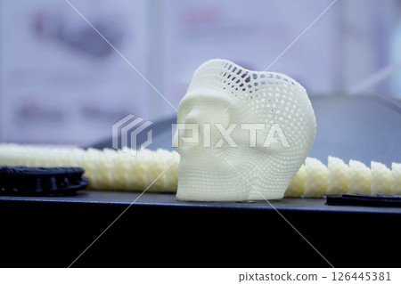 Small prototype of human skull 3D printed from molten white plastic on surface close-up. Three-dimensional model. Modern new printing manufacturing industry. Additive progressive medical technology. Small prototype of human skull 3D printed from molten white plastic on surface close-up. Three-dimensional model. Modern new printing manufacturing industry. Additive progressive medical technology. 126445381