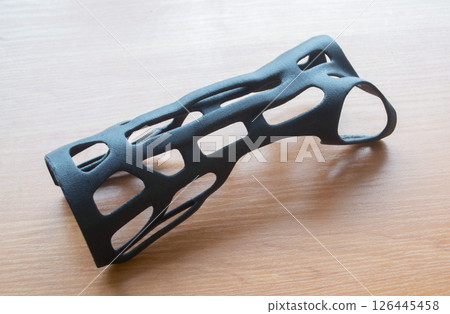 Hand splint corset prosthesis printed on 3D printer from molten black plastic powder on table. Medical orthosis fixator plastic overlay created on 3D printer. New modern medical 3D printing technology 126445458