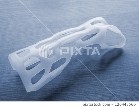 Hand splint corset prosthesis printed on 3D printer from molten white plastic powder on table. Medical orthosis fixator plastic overlay created on 3D printer. New modern medical 3D printing technology 126445560