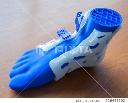 Prosthesis printed on a 3D printer from molten plastic on a plastic foot. Prototype of medical prosthesis for foot created on 3D printer. Medical orthosis, fixator, splint corset langet from plastic Prosthesis printed on a 3D printer from molten plastic on a plastic foot. Prototype of medical prosthesis for foot created on 3D printer. Medical orthosis, fixator, splint corset langet from plastic 126445602
